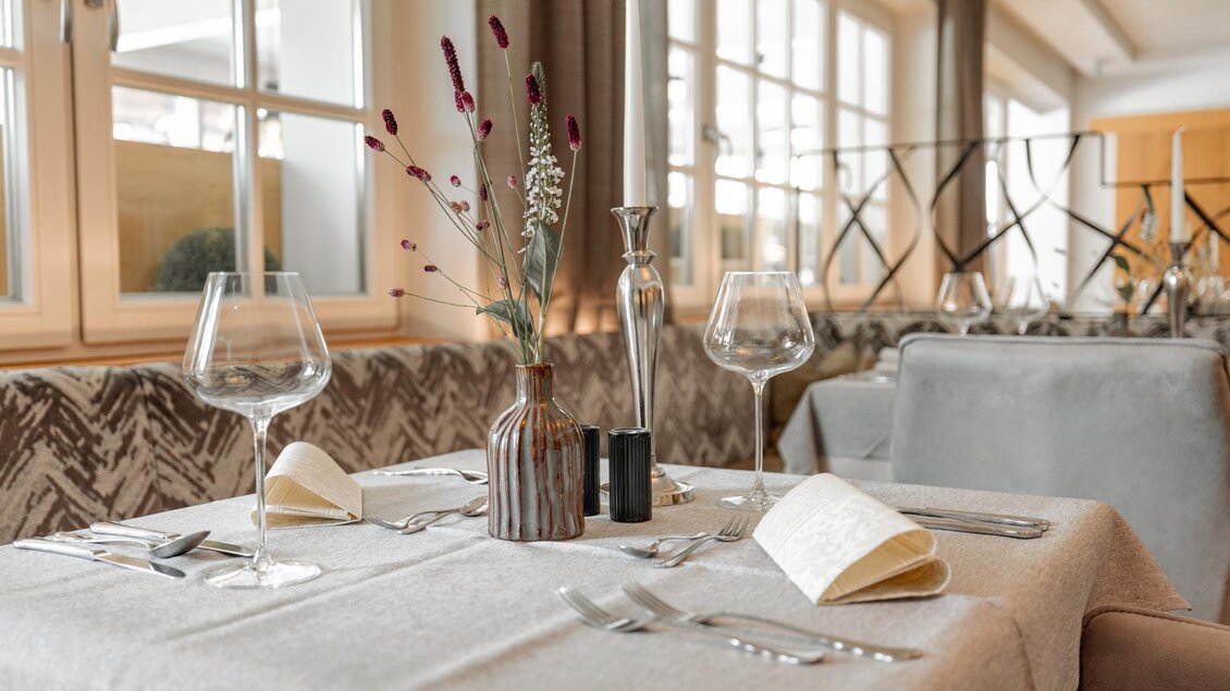 Ein eleganter Tisch in einem Restaurant, dekoriert mit einem kleinen Blumenstrauß und gestylten Gläsern. Helle Fenster sorgen für eine freundliche Atmosphäre. | © Vison