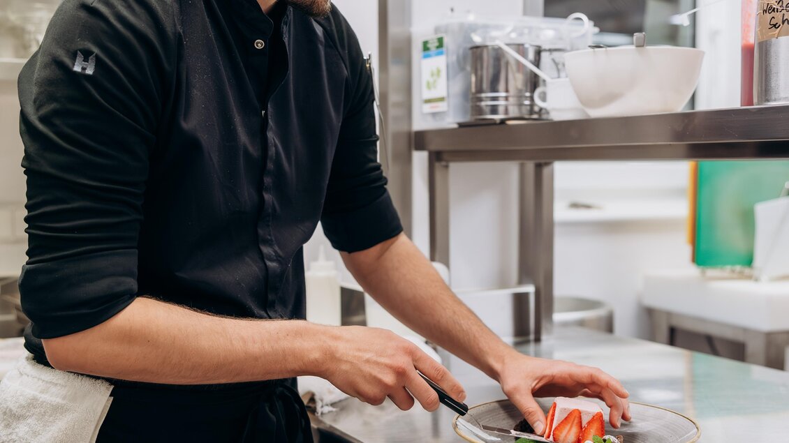 Ein Koch bereitet ein Gericht in einer modernen Küche vor. Er schneidet sorgfältig frisches Gemüse auf einem Teller.