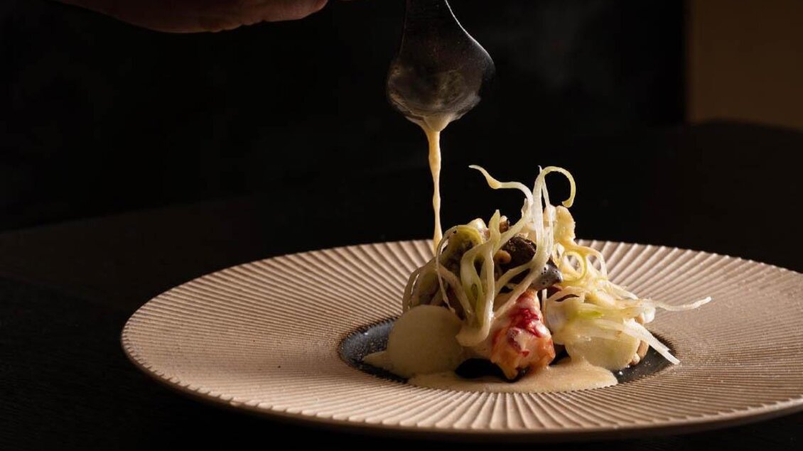 Hand träufelt helle Sauce über angerichtetes Gericht mit Gemüse im Artis Graz. | © Sebastian Knapp