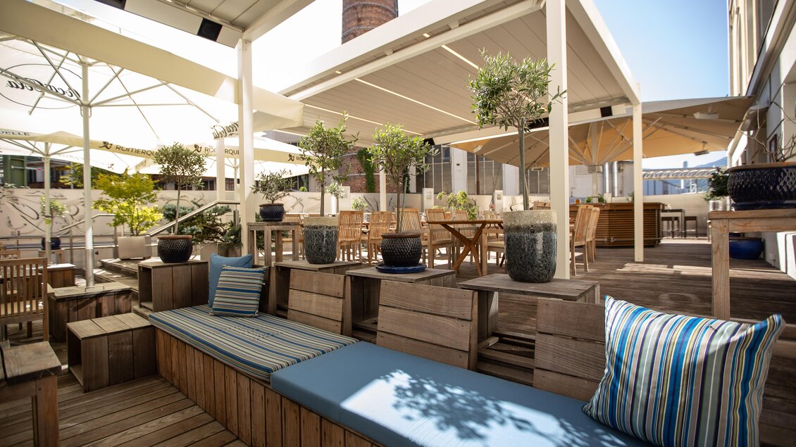 Eine moderne Terrasse mit Holzbelag und gemütlichen Sitzgelegenheiten. Überdachte Bereiche bieten Schatten, während Pflanzen für eine angenehme Atmosphäre sorgen. | © Hotel Böhlerstern