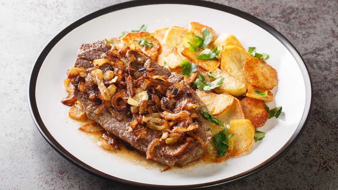 Ein saftiges Rindersteak mit Zwiebeln und knusprigen Bratkartoffeln. Das Gericht ist mit frischen Kräutern garniert. | © Hotel Böhlerstern