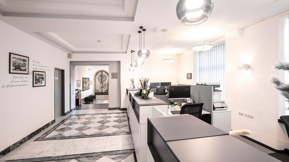 Ein modernes Büro mit einem eleganten Fußboden und heller Beleuchtung. Die Empfangstheke ist gut organisiert, während die Büroräume im Hintergrund sichtbar sind.