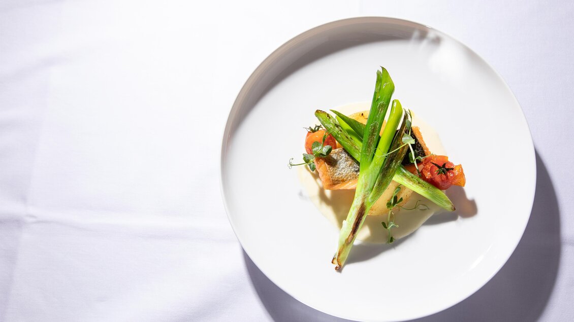 Ein eleganter Teller mit frischen Zutaten, darunter grüne Zwiebeln und Tomaten. Die Speise ist kunstvoll angerichtet und sieht appetitlich aus. | © Hotel Böhlerstern
