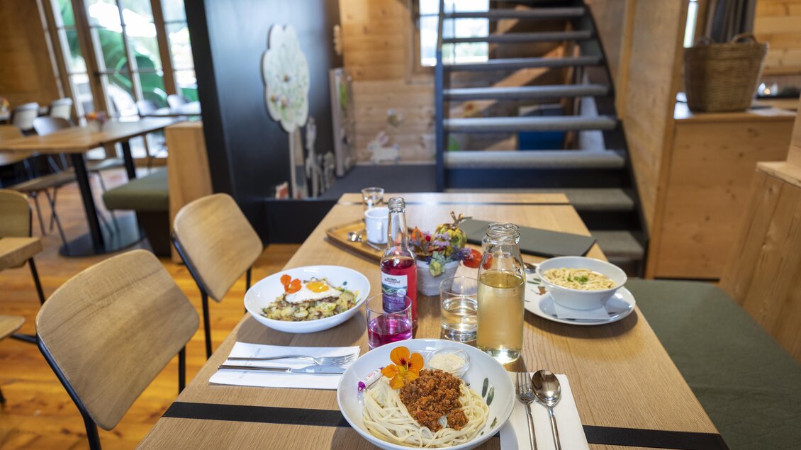 Ein gemütlicher Tisch in einem Restaurant mit zwei Schalen Pasta und einem Getränk. Im Hintergrund sind Holzregale und eine Treppe zu sehen. | © Waldpark Hochreiter