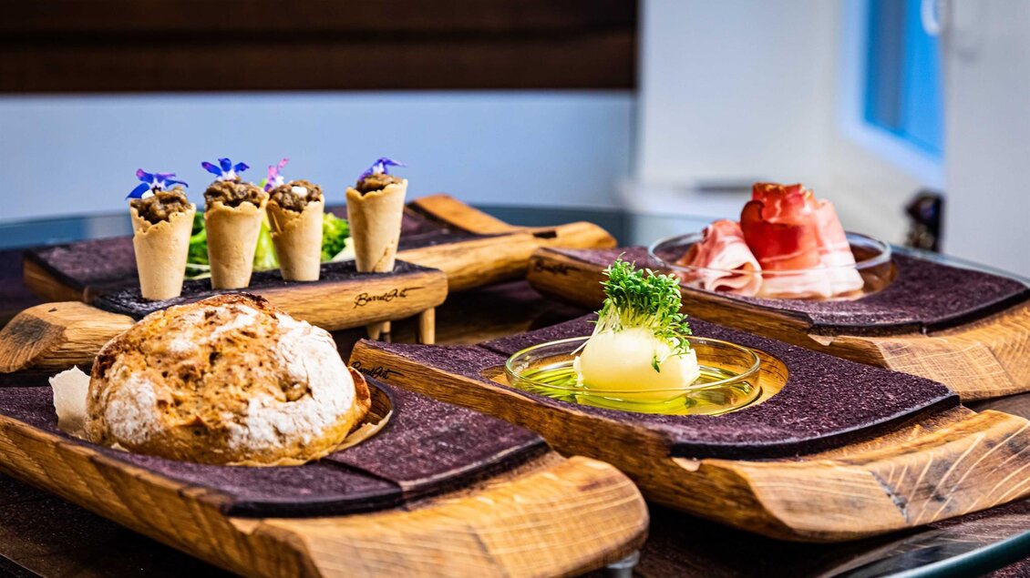 Ein ansprechendes Gourmet-Gericht auf Holzplatten, bestehend aus frischem Brot, kleinen Snacks in Waffelhülsen und verschiedenen Fleischsorten. Die Präsentation ist elegant und ansprechend, ideal für ein feines Abendessen. | © Broadmoar