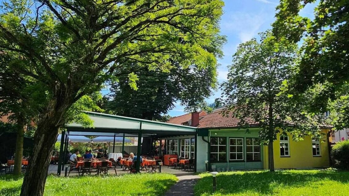 Ein einladendes Café unter Bäumen mit einer Terrasse im Freien. Der Himmel ist klar und die Umgebung ist grün und gepflegt. | © Kastanienlaube