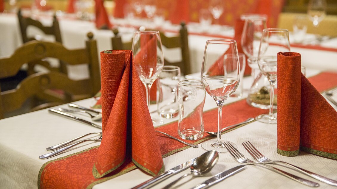 Ein eleganter Tisch mit rotem Tischset und gefalteten Servietten. Gläser und Besteck sind sorgfältig arrangiert. | © Gollner