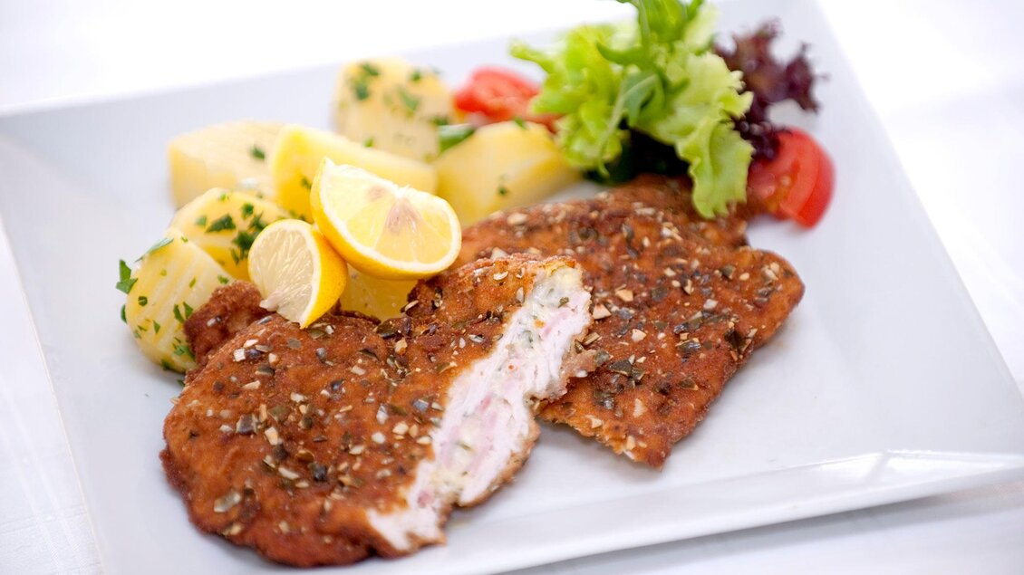 Ein Teller mit paniertem Fleisch, serviert mit Kartoffeln, frischen Salat und Zitronenscheiben. Die Farben sind appetitlich und das Gericht sieht lecker aus. | © Gollner