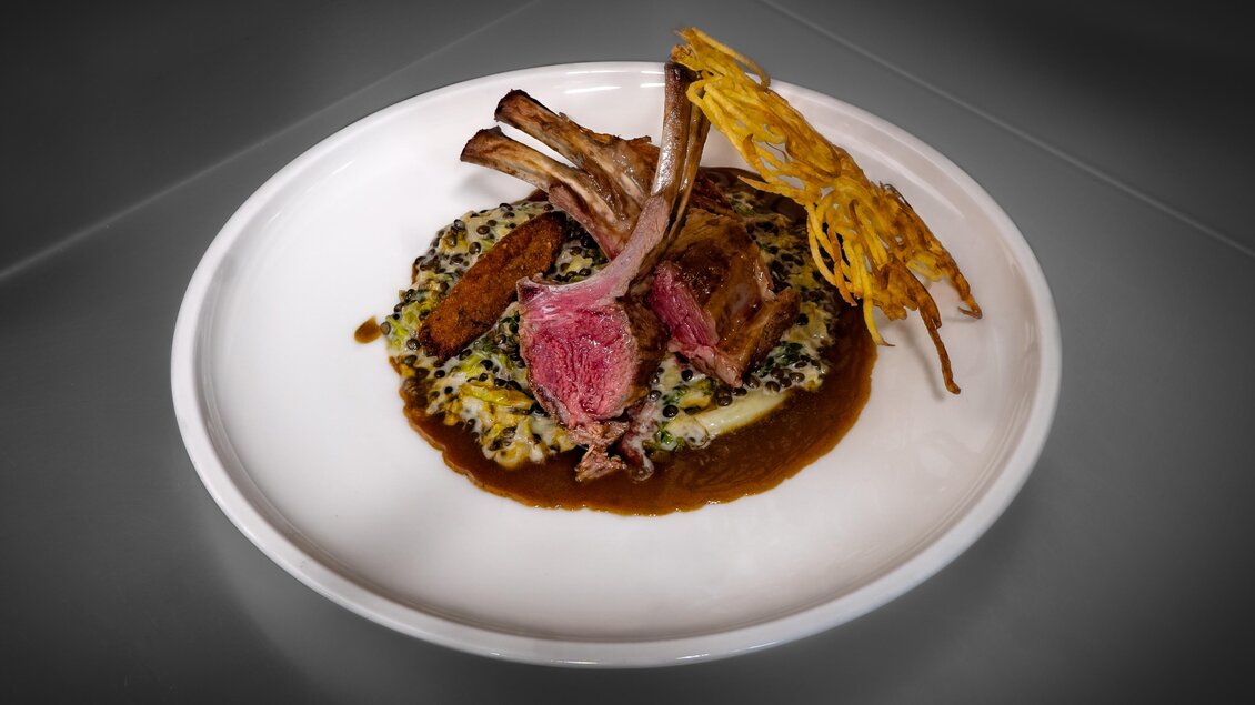 Ein kunstvoll angerichteter Teller mit Lammkoteletts auf einem Bett aus Risotto. Dazu eine herzliche Sauce und knuspriges Gemüse. | © Gollner