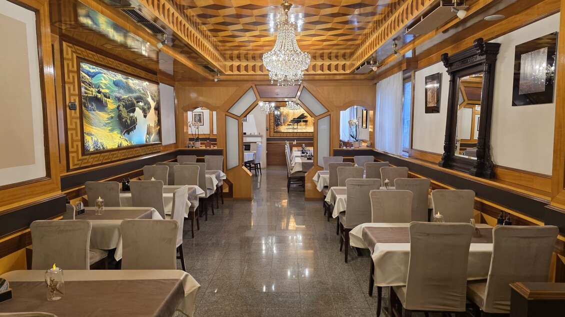 Ein elegantes Restaurant mit Holzverkleidung und einer modernen Decke. Die Tische sind ordentlich gedeckt und es hängt ein schöner Kronleuchter.