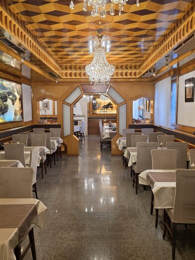 An elegant restaurant with wood paneling and a modern ceiling. The tables are neatly set, and there is a beautiful chandelier hanging.