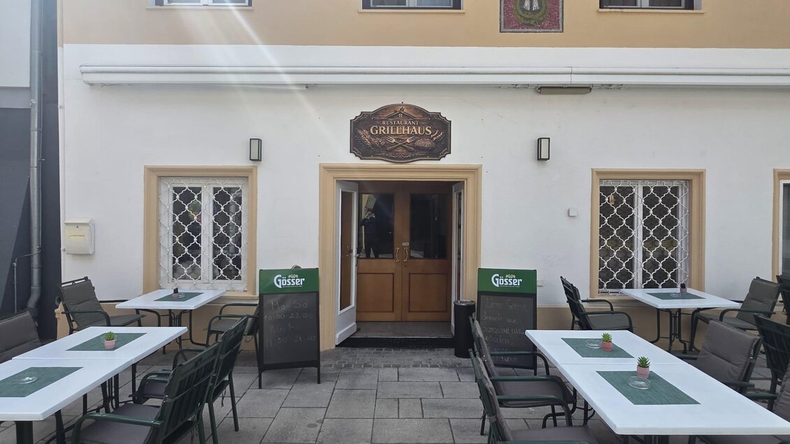 Ein gemütliches Restaurant mit mehreren Tischen im Freien. Die Fassade ist hell und einladend, mit einem Schild über dem Eingang. | © Grillhaus