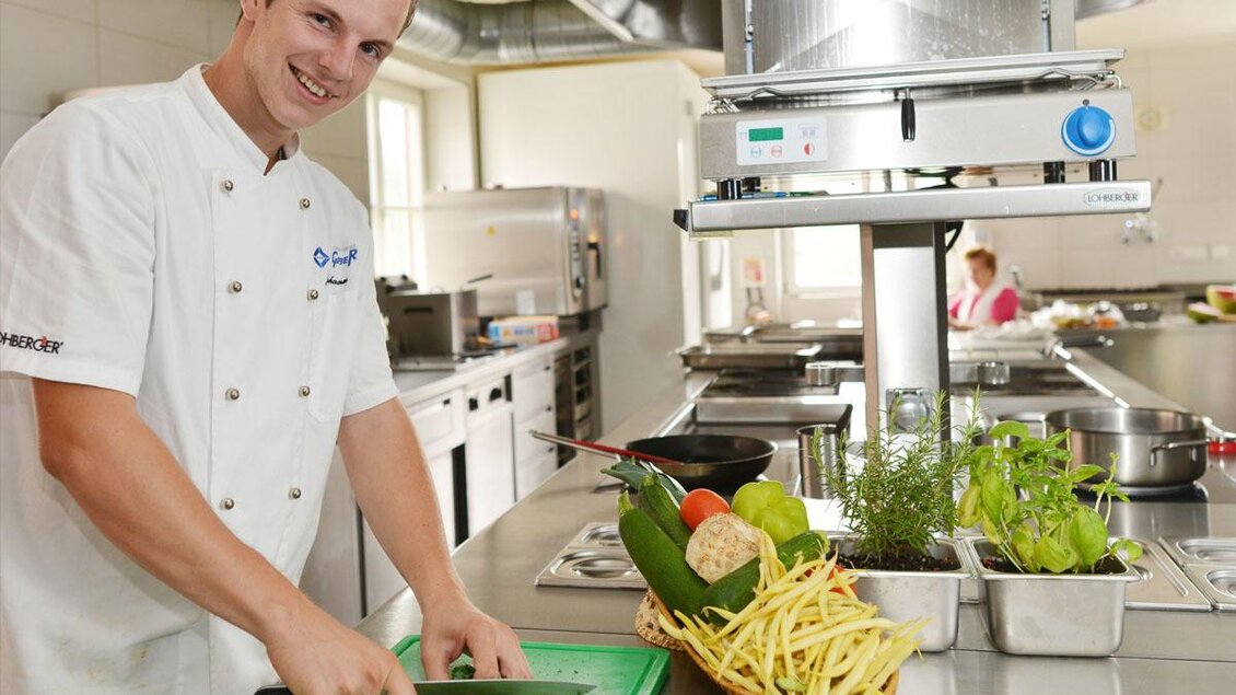 Ein Koch schneidet frische Kräuter in einer modernen Küche. Obst und Gemüse sind auf der Arbeitsfläche angerichtet. | © Hotel-Restaurant Gruber