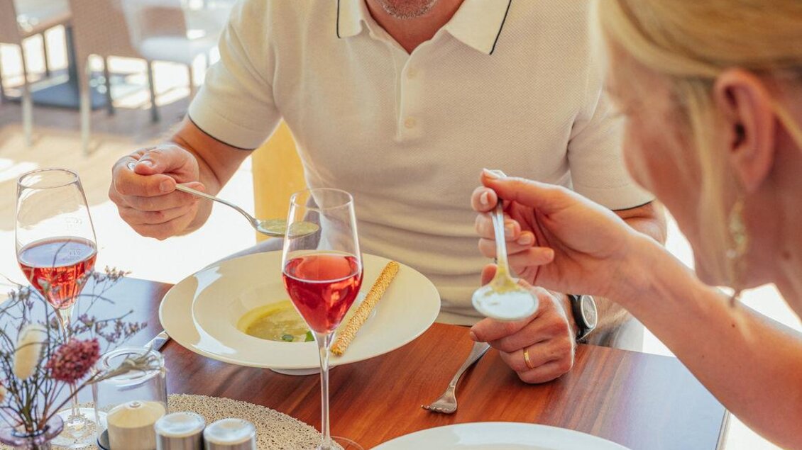 Ein Paar genießt ein Essen in einem hellen Restaurant. Auf dem Tisch stehen zwei Teller mit Suppe und Drinks. | © VLMMEDIA