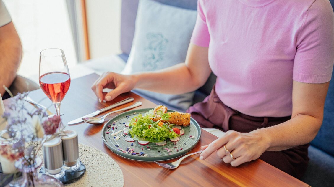 Ein Tisch mit einem Teller Salat und einer Rolle. Neben dem Essen steht ein Glas mit einem roten Getränk. | © N. Ulrich
