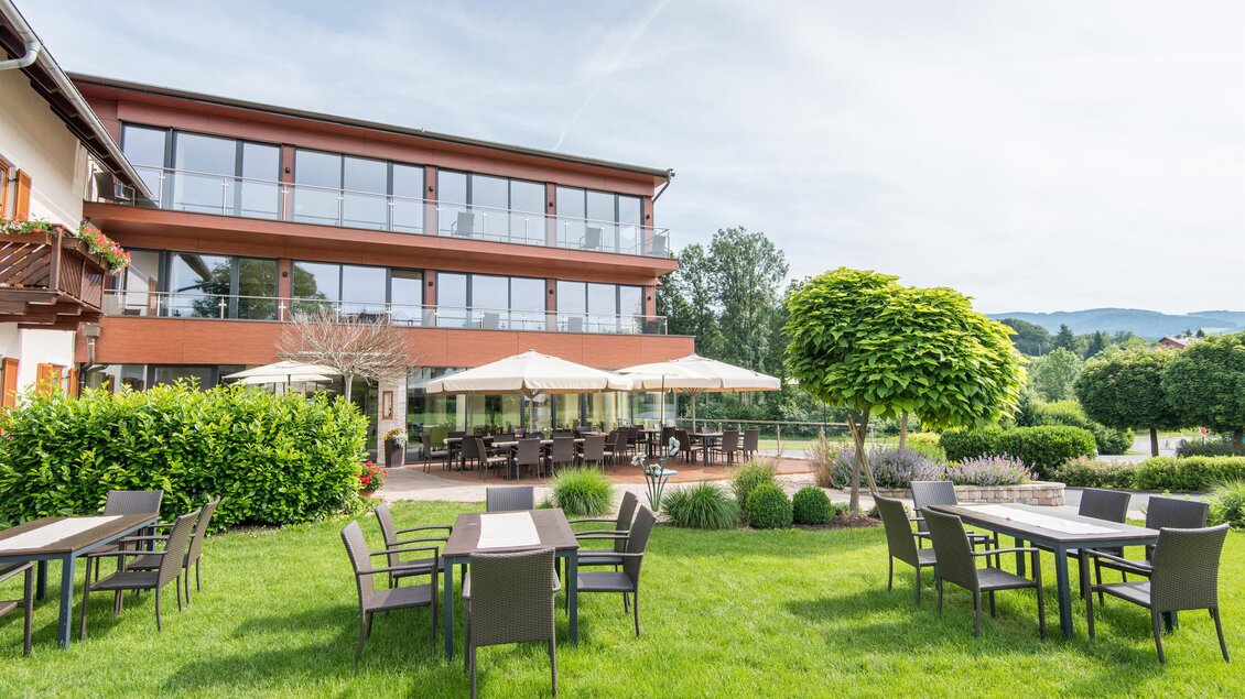 Ein modernes Gebäude mit großen Fenstern und einem großzügigen Gartenbereich. Tische und Stühle stehen im Freien, umgeben von gepflegtem Grün. | © Helmut Schweighofer