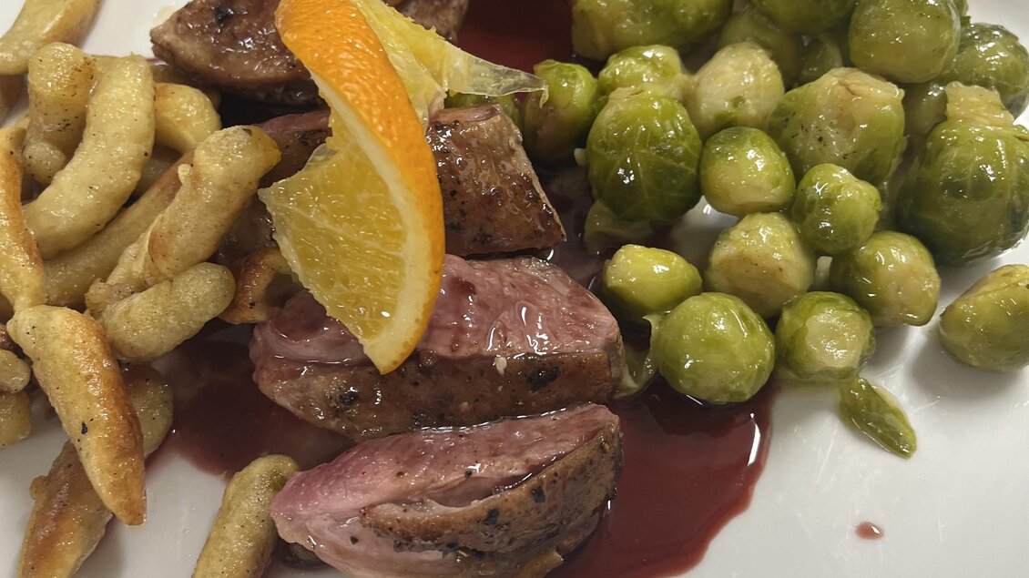 Ein Teller mit gebratenem Fleisch, umgeben von Bratkartoffeln und Rosenkohl. Dazu gibt es eine Scheibe Pfirsich und eine fruchtige Sauce. | © Restaurant Hasenwirt