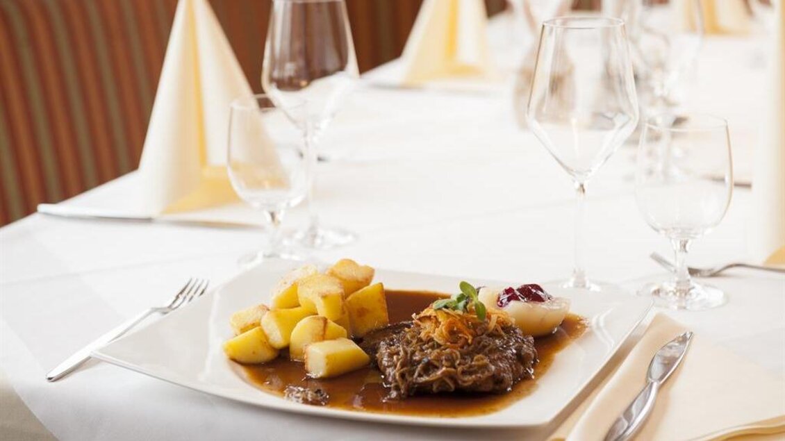 Ein elegantes Tischgedeck mit einem köstlichen Fleischgericht, Kartoffeln und Beilagen. Klare Gläser und dekorative Servietten runden das Bild ab. | © Thomas Wasle
