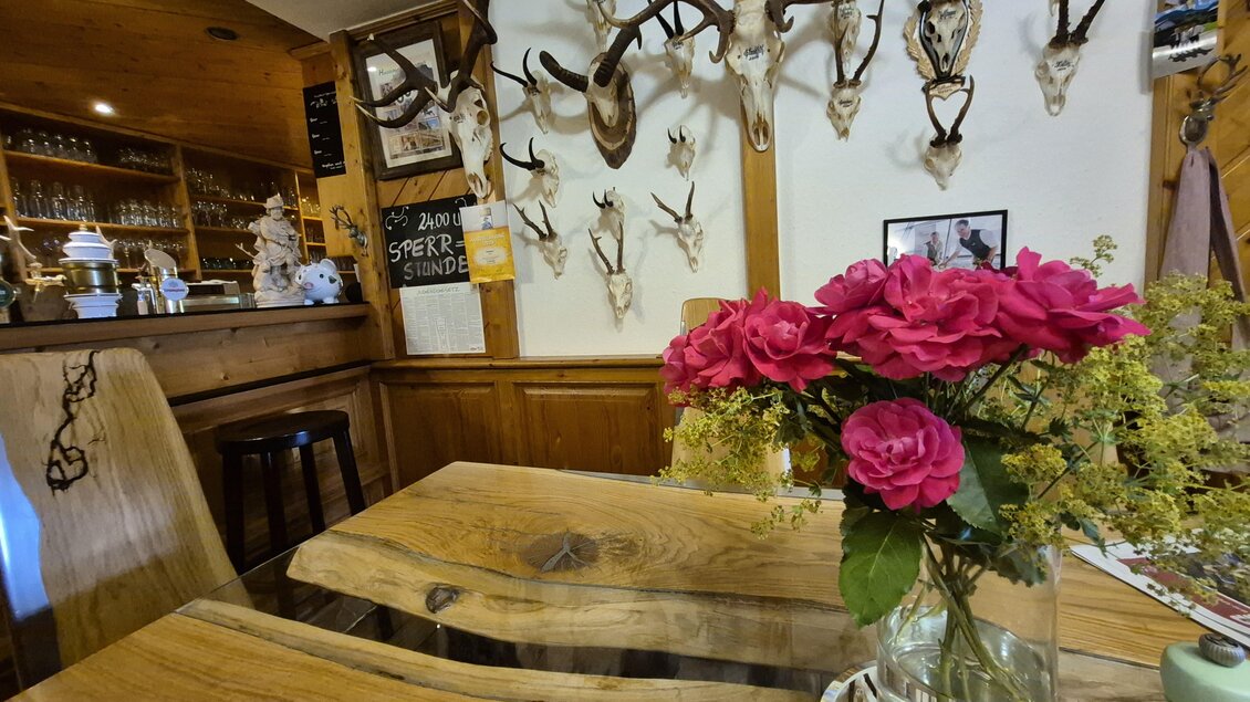 Ein gemütliches Restaurant mit Holzmöbeln und einer Blume in einer Vase. An der Wand hängen Geweihe, was eine rustikale Atmosphäre schafft. | © TV Hochsteiermark
