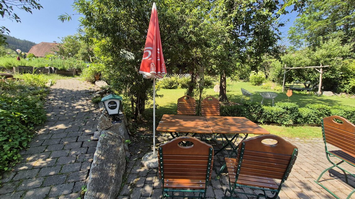 Ein gemütlicher Außenbereich mit einem Tisch und Stühlen unter einem Sonnenschirm. Die Umgebung ist grün und einladend, ideal zum Entspannen. | © TV Hochsteiermark