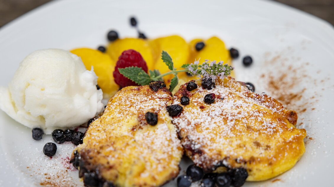 Ein köstliches Dessert mit frisch zubereiteten Pfannkuchen, Früchten und einer Kugel Eis. Das Gericht ist mit Puderzucker und Beeren garniert. | © 5komma5sinne