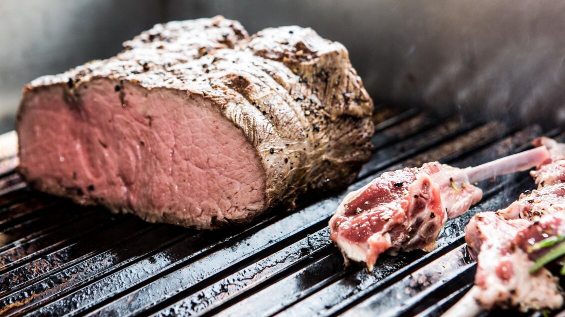 Ein Stück saftiges Roastbeef liegt auf dem Grill. Daneben sind einige Fleischstücke zum Grillen vorbereitet.