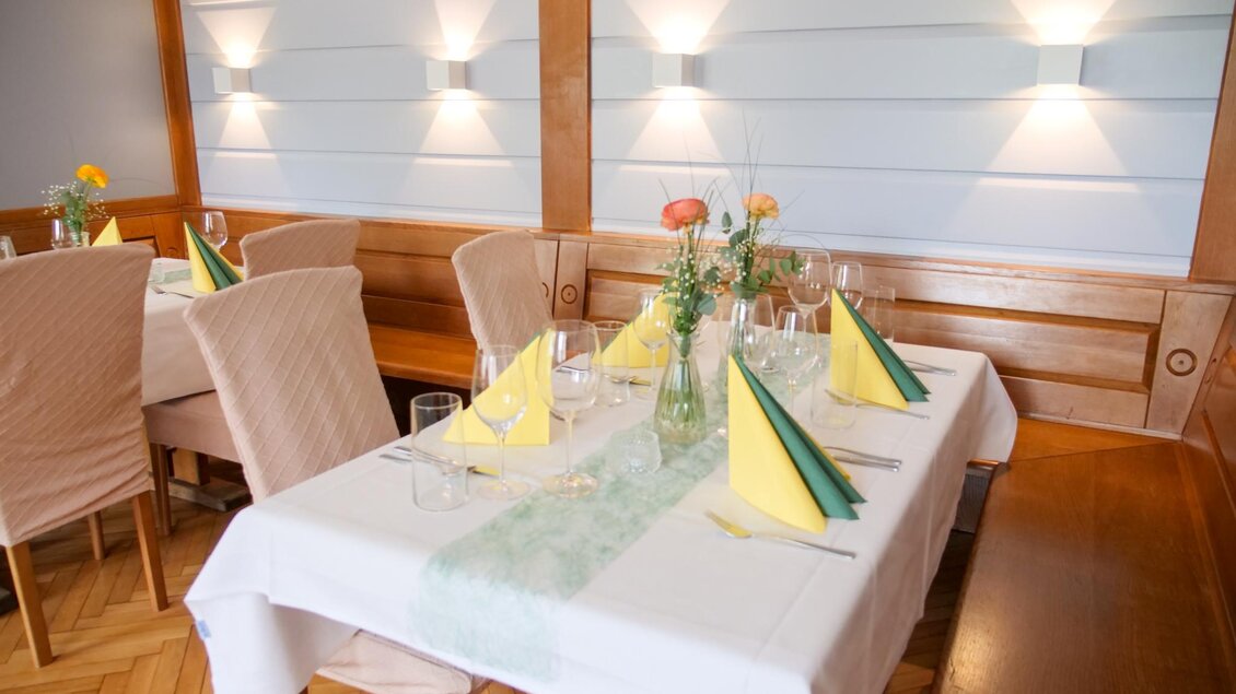 Ein elegant gedeckter Tisch in einem Restaurant mit gelben und grünen Servietten. Die gemütliche Atmosphäre wird durch sanftes Licht und frische Blumen ergänzt. | © Kirchenwirt Stubenberg