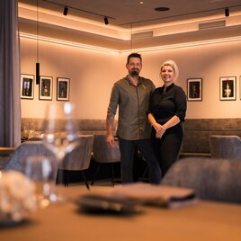 Ein modernes Restaurant mit stilvollem Design. Zwei Personen stehen lächelnd im Vordergrund. | © Nadine Geuter- Black Ink Production