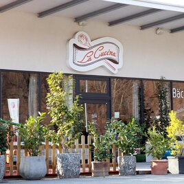 Ein einladendes Restaurant mit dem Namen "La Cucina" und einer Bäckerei. Die Fassade ist von vielen Pflanzen in Töpfen umgeben. | © TV Region Graz - Lunghammer