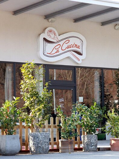 An inviting restaurant named "La Cucina" with a bakery. The facade is surrounded by many potted plants. | © TV Region Graz - Lunghammer