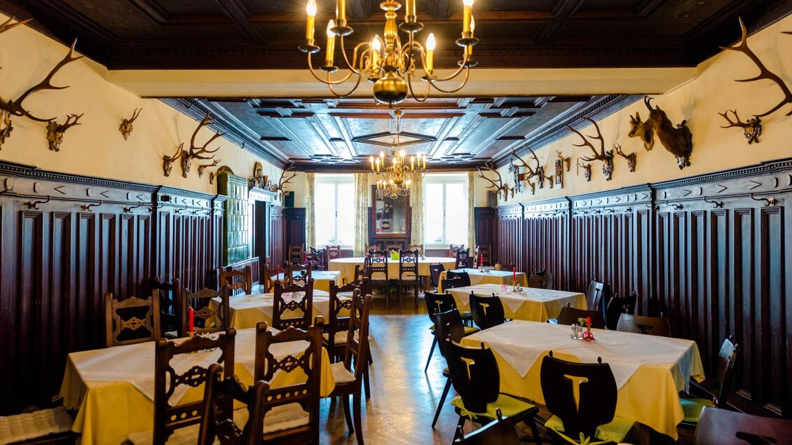 Ein traditionelles Restaurant mit Holzwänden und mehreren Tischen. Antlers schmücken die Wände und eine große Deckenlampe sorgt für Beleuchtung. | © Landhotel  Groggerhof