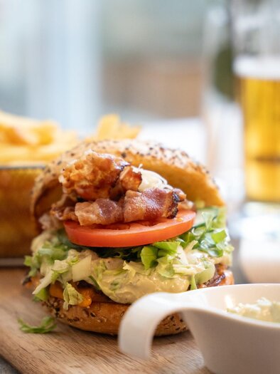Burger with vegetables and bacon, served with fries and a beer on a wooden table in Schachenwald | © Schachenwald - Wolfgang Hummer