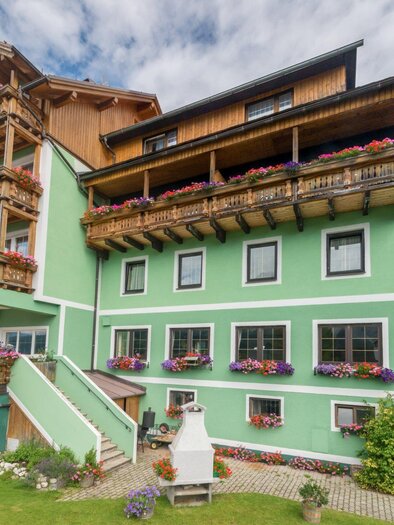 Ein farbenfrohes Gebäude im Landhausstil mit Balkonen und blühenden Pflanzen. Die Fassade ist grün, umgeben von einer gepflegten Gartenanlage. | © Restaurant Schwaiger