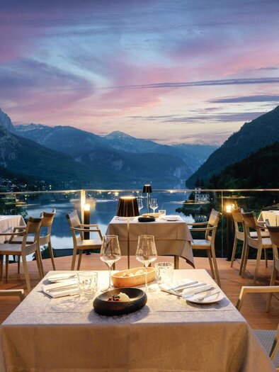 An elegant restaurant with tables on a terrace. In the background, mountains and a beautiful sunset are visible. | © Mondi Resort
