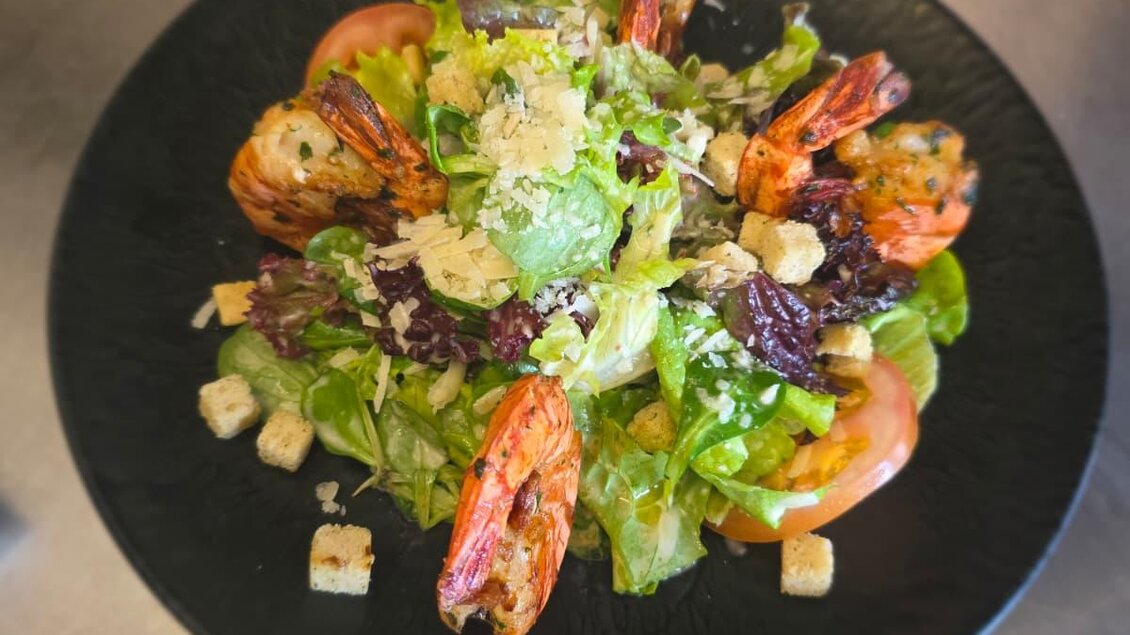 Ein frischer Salat mit Garnelen, gemischtem Grün und Tomatenscheiben. Der Salat ist mit Croutons und Parmesan bestreut.