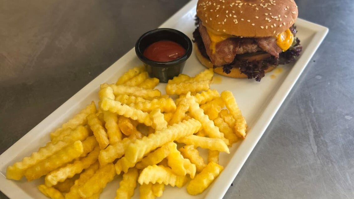 Ein saftiger Burger mit Käse und einem Sesam-Brötchen, serviert mit knusprigen Pommes frites. Dazu gibt es eine kleine Schale Ketchup.