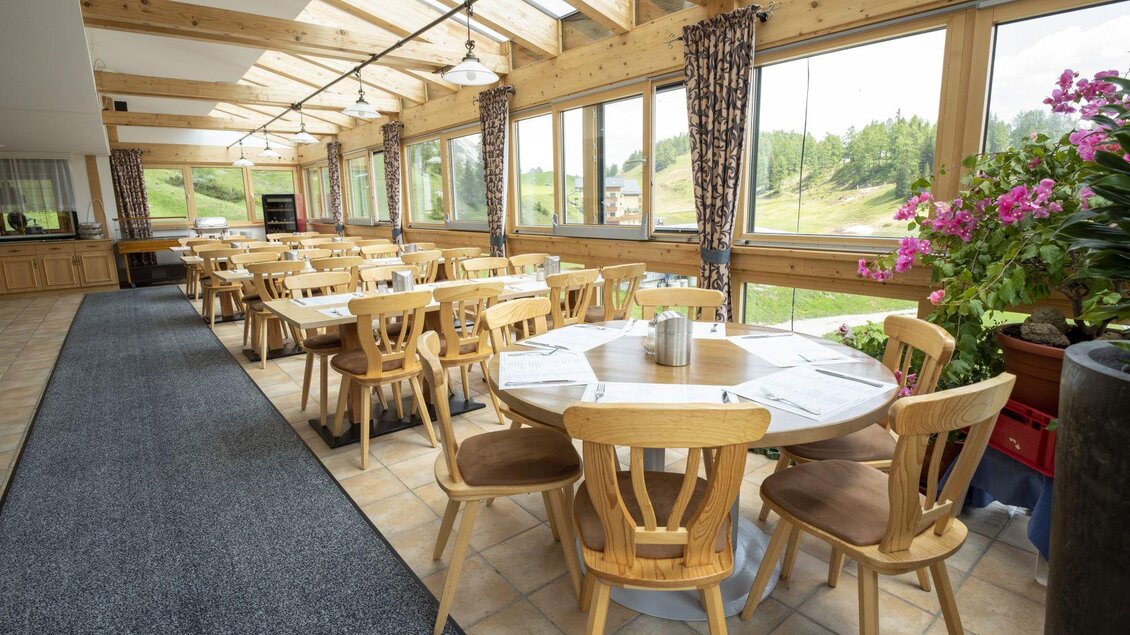 <p>Der Wintergarten des Restaurants mit Holzstühlen und großen Fenstern. Der Raum ist hell und freundlich, umgeben von Pflanzen und einer schönen Aussicht.</p> | © Hotel Alpen Arnika
