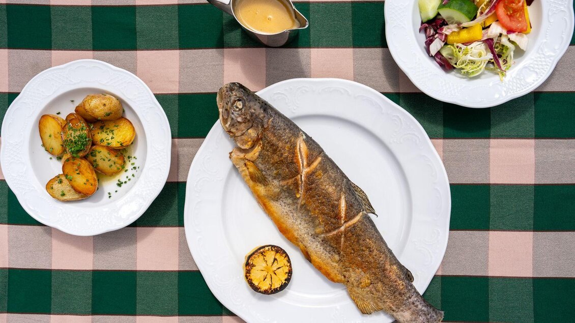 <p>Ein gegrillter Saibling auf einem weißen Teller, dazu Kartoffeln und ein frischer Salat. p> | © Hotel Alpen Arnika