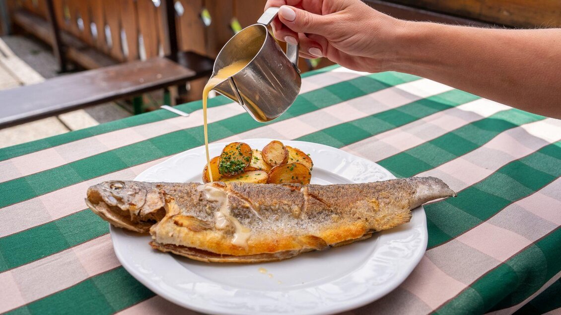 <p>Ein frisch zubereiteter Fisch auf einem weißen Teller, serviert mit Kartoffeln und Gemüse.</p> | © Hotel Alpen Arnika