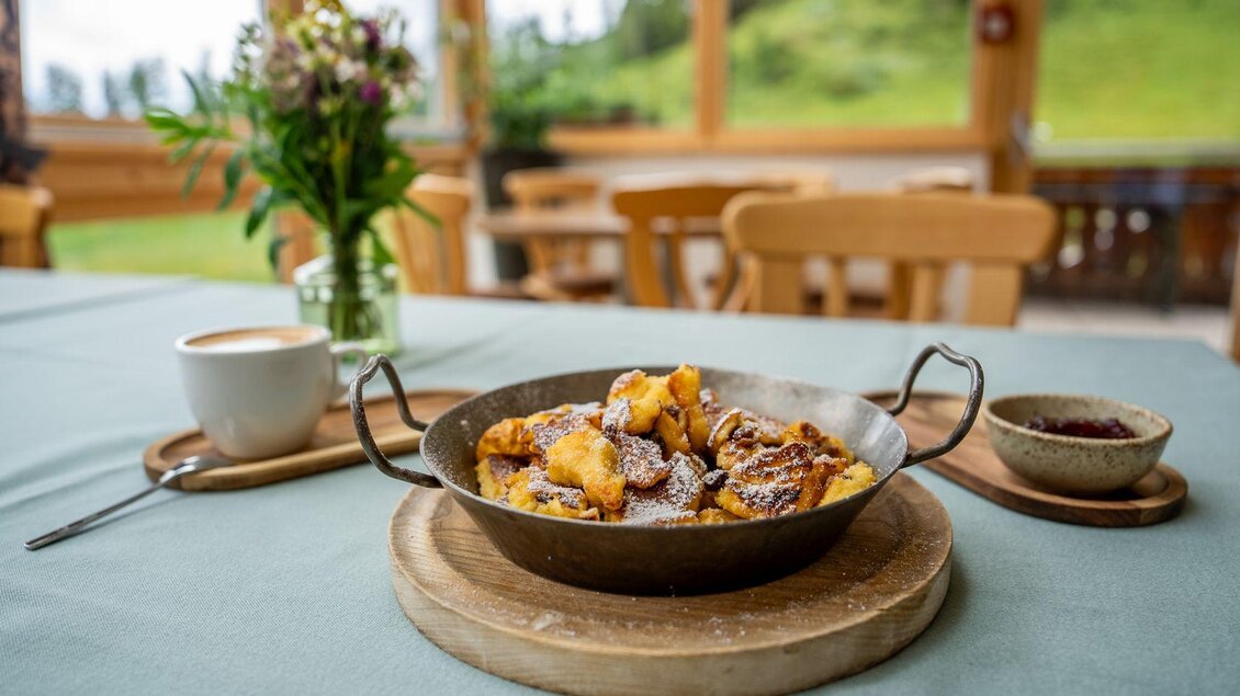 <p>Kaiserschmarrn in einer Pfanne, serviert mit Puderzucker. Im Hintergrund sind frische Blumen und eine gemütliche Umgebung zu sehen.</p> | © Hotel Alpen Arnika