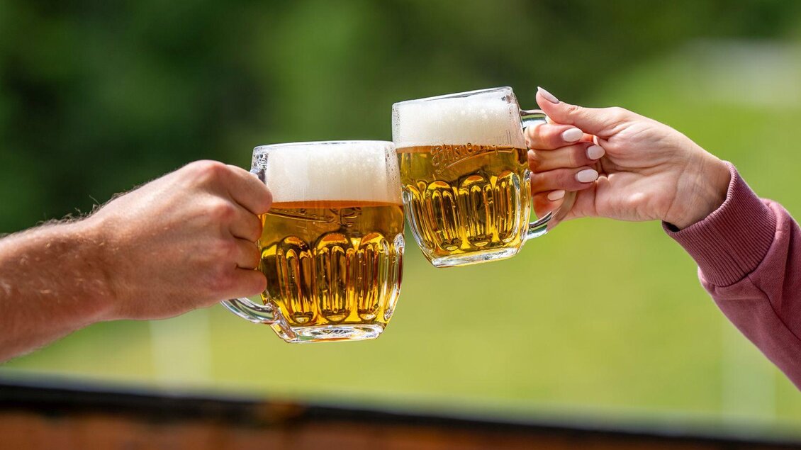 <p>Zwei Bierkrüge stoßen an. Im Hintergrund ist eine grüne Landschaft zu sehen.</p> | © Hotel Alpen Arnika