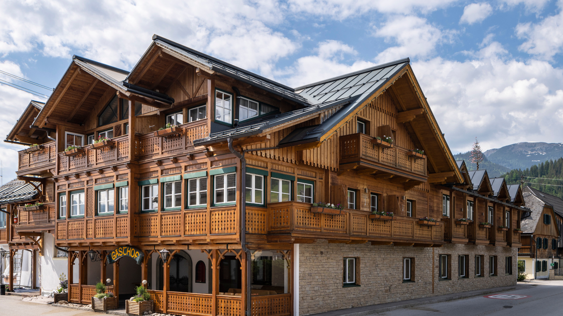 Eine Außenansicht des Restaurants im Kanzler Wander- und Wellnesshotel. Es ist ein traditionelles Holzhaus mit vielen Fenstern und Holzverzierungen im Ausseer Stil, geschmückt mit bunten Balkonblumen. | © Gasthaus Kanzler