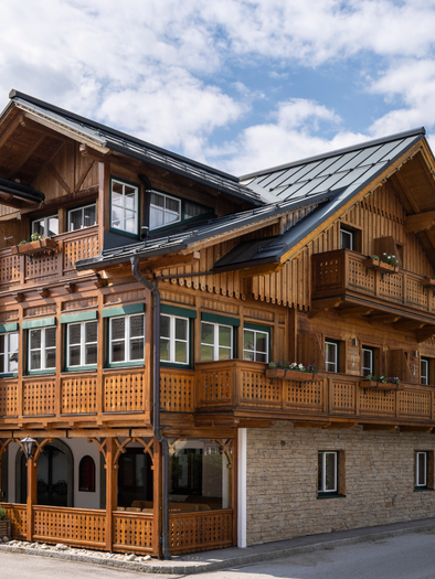 Eine Außenansicht des Restaurants im Kanzler Wander- und Wellnesshotel. Es ist ein traditionelles Holzhaus mit vielen Fenstern und Holzverzierungen im Ausseer Stil, geschmückt mit bunten Balkonblumen. | © Gasthaus Kanzler