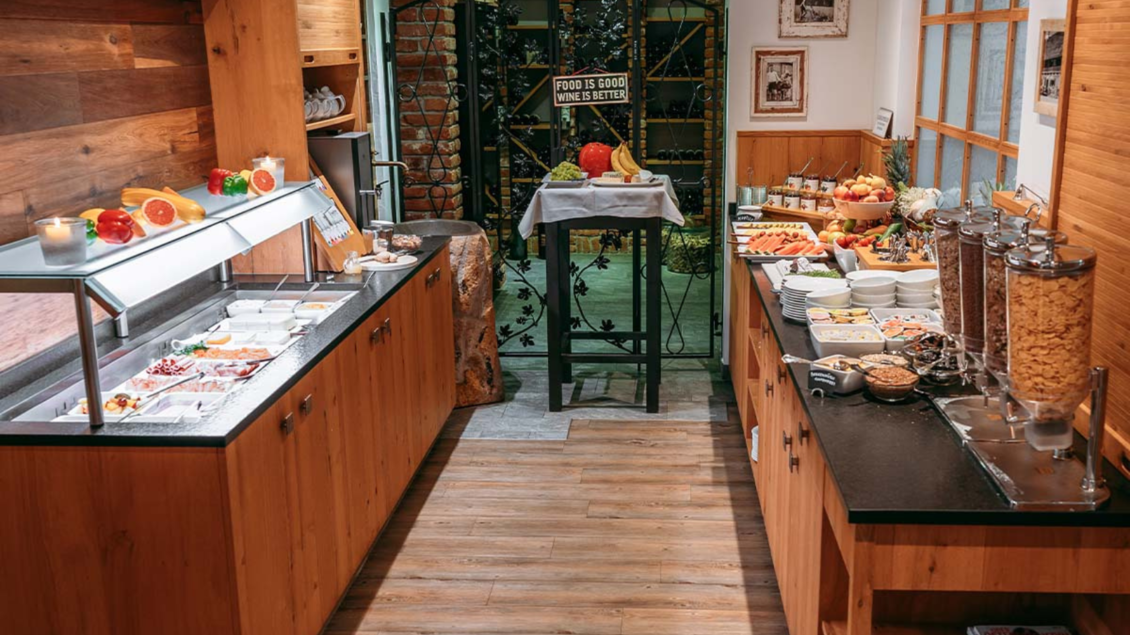 Ein einladender Frühstücksraum im Kanzler Wander- und Wellnesshotel mit Holzregalen und einer Auswahl an frischem Obst, Müsli und Aufschnitt. Auf einem Tisch stehen weitere Speisen bereit, um den Morgen zu genießen. | © Gasthaus Kanzler