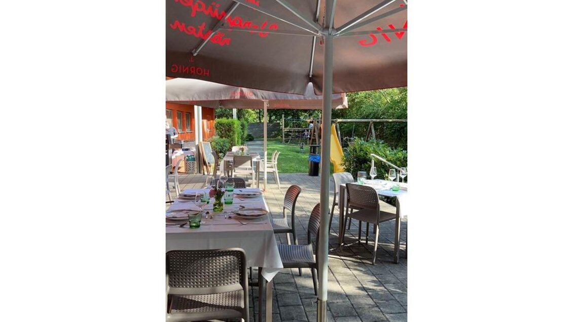 Ein gemütliches Restaurant im Freien mit Tischen und Stühlen unter einem Sonnenschirm. Die Umgebung ist grün und einladend. | © JUFA Hotel Leibnitz
