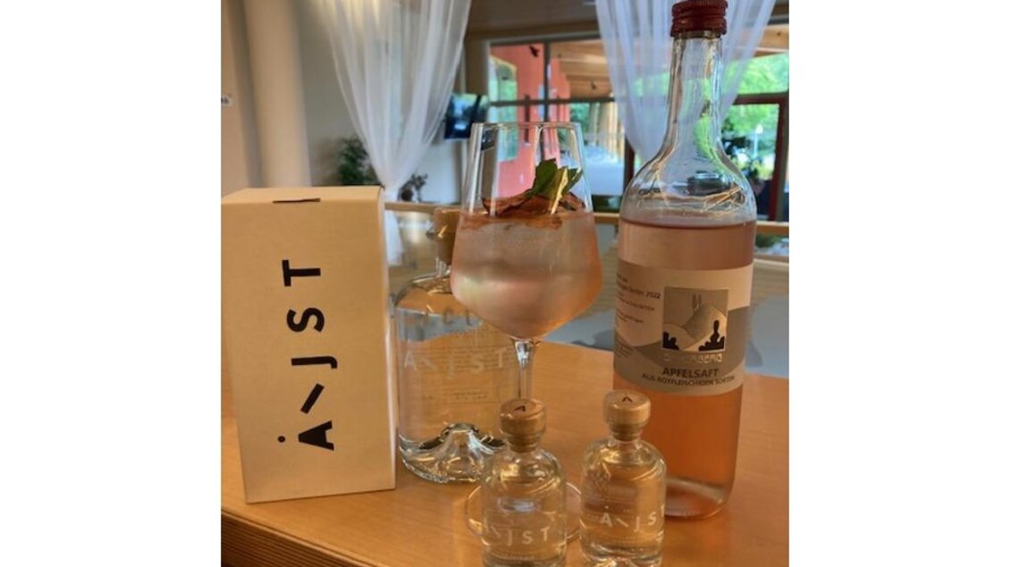 Ein elegantes Getränk in einem Glas mit einer Zitrusscheibe und Minze. Darum herum stehen verschiedene Flaschen und eine schlichte Box. | © JUFA Hotel Leibnitz