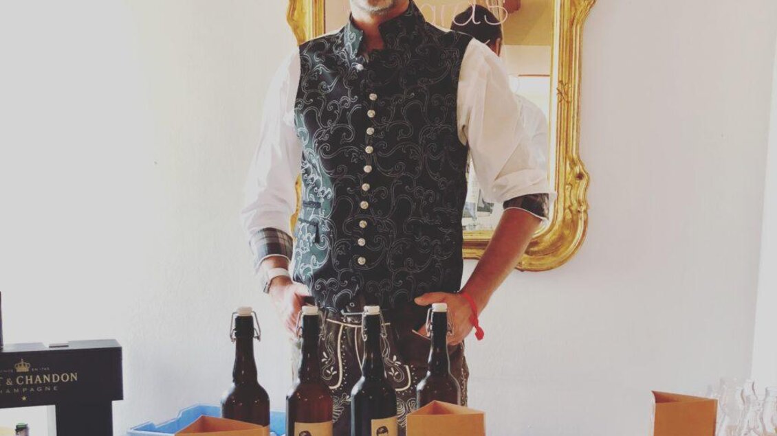 Ein lächelnder Mann steht an einem Tisch mit mehreren Flaschen Bier. Der Tisch ist dekoriert mit grünen Pflanzen und Papiertüten. | © Richards Bieratelier