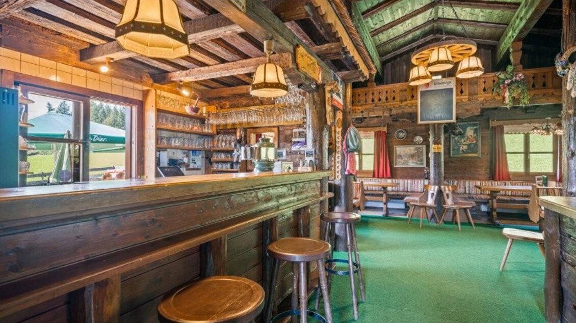 Ein gemütlicher Innenraum eines rustikalen Bars mit holzverkleideten Wänden und einem langen Tresen. Das Licht ist warm und freundlich, mit Sitzmöglichkeiten verteilt im Raum. | © Alwin Strasser