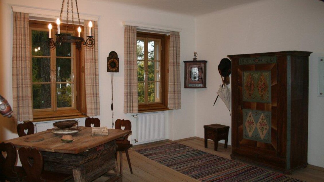 Ein gemütlicher Essbereich mit einem Holztisch und Stühlen. An den Wänden hängen Vorhänge und es gibt einen großen Schrank sowie eine ausgeraumte Holzdecke. | © TV Hochsteiermark, Maria Steindl