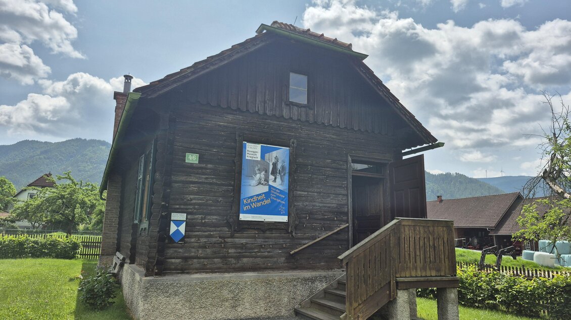 Ein traditionelles Holzhaus steht in einer grünen Umgebung. Die Sonne scheint und der Himmel ist teilweise bewölkt. | © TV Hochsteiermark/Andrea Stelzer